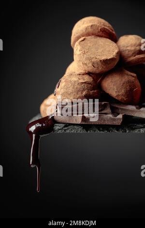 Deliziosi tartufi di cioccolato e gocce di salsa di cioccolato su sfondo nero. Foto Stock