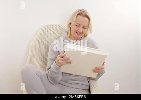 La donna sta sfogliando un album con pagine vuote. La mano della donna gira lentamente la pagina di un taccuino pulito del libro con le pagine beige. Guardando attraverso una f Foto Stock