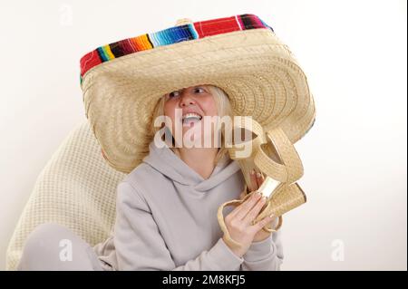 mexican Hat Dancing Dancing maturo donna messicana in sombrero cappello su sfondo bianco donna adulta tiene belle scarpe di paglia con tacco alto nelle sue mani, Foto Stock