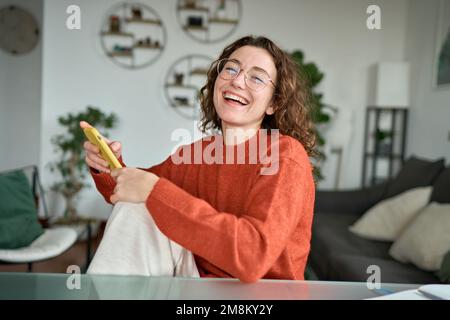 Felice giovane donna ridendo seduto a casa utilizzando il telefono cellulare. Foto Stock