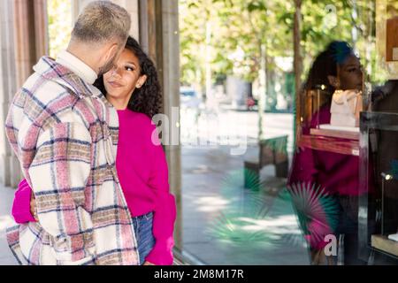 Una giovane coppia, passeggiando per una strada cittadina, in piedi in una vetrina, guardando nella finestra di un negozio. Foto Stock