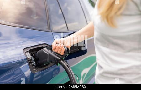 Donna che inserisce un connettore di ricarica DC CCS2 EV nella presa elettrica per auto della stazione di ricarica, dell'hypercharger o del Supercharger. Caricare l'elettromobilità CO Foto Stock