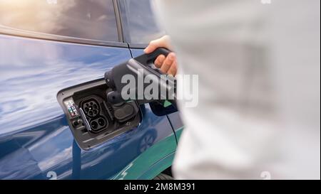 Donna che inserisce un connettore di ricarica DC CCS2 EV nella presa elettrica per auto della stazione di ricarica, dell'hypercharger o del Supercharger. Caricare l'elettromobilità CO Foto Stock