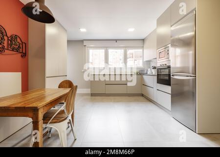 Zona ufficio di una cucina in un appartamento con i toni del grigio nell'arredamento e un tavolo quadrato in legno e una panca per sedersi nell'angolo, triplo vento Foto Stock