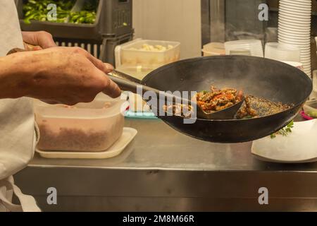 Uno chef asiatico friggerà il manzo caramellato in un wok fumante con un mestolo grande Foto Stock