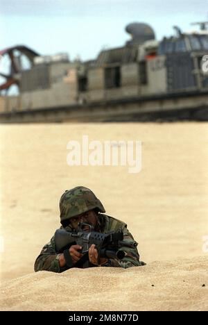 US Marine Corps LCPL Donald Retreage of Co. A, 1st Light Armored Reconnaissance, Camp Pendleton, California, attende il segnale per avanzare dalla sua posizione perimetrale durante l'esercitazione RIMPAC '98 Beach assalto. Dietro di lui c'è un Landing Craft, Air Cushion veicolo che porta più Marines in spiaggia. Subject Operation/Series: RIMPAC '98 base: Barking Sands, Kauai Stato: Hawaii (HI) Paese: Stati Uniti d'America (USA) Foto Stock