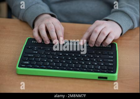 Un uomo cieco utilizza un computer con un display Braille e una tastiera per computer. Dispositivo incluso. Foto Stock