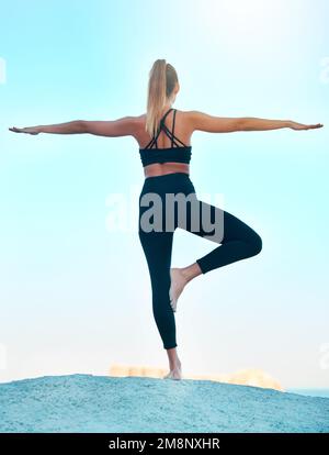 Retroguarante bella donna che pratica yoga esercizio sulla spiaggia. Giovane atleta femminile che si allunga mentre si allenano fuori. Trovare la pace interiore e. Foto Stock