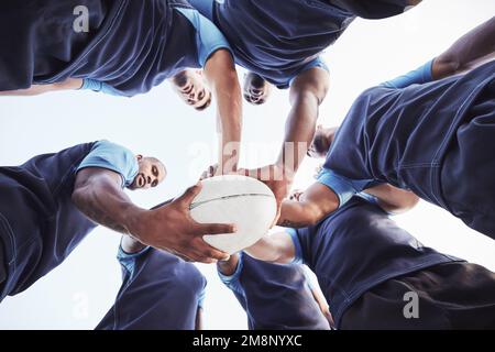 Sotto diversi gruppi di giocatori di rugby in piedi in un huddle insieme fuori su un campo. Giovani atleti maschi che guardano seri e concentrati mentre si sono accoccolati Foto Stock