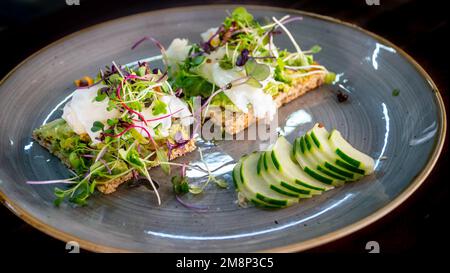 una sana colazione a base di uova in camicia con avocado su toast e guarnite con cetriolo a fette Foto Stock