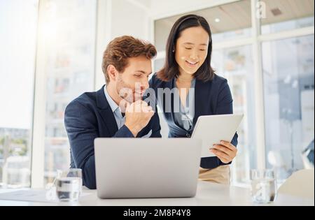 Due giovani e felici colleghi che lavorano insieme su un tablet digitale in ufficio. Donna d'affari asiatica fiduciosa che mostra sorridente caucasico Foto Stock