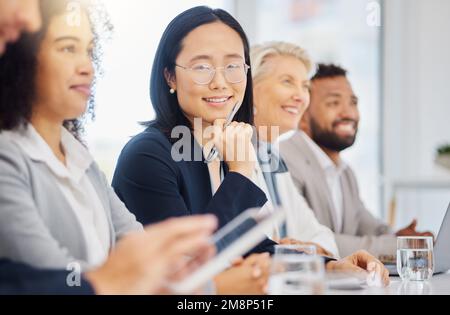 Ritratto di felice giovane donna d'affari asiatica che ascolta la presentazione durante la riunione in ufficio sala riunioni con diversi colleghi. Sorridente Foto Stock
