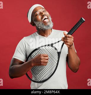 Un felice uomo afroamericano maturo in piedi contro uno sfondo rosso in studio in attesa che la sua partita abbia inizio. Un uomo nero sorridente che si sente in forma e. Foto Stock
