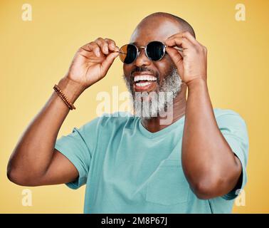 Felice uomo afroamericano maturo in piedi da solo su sfondo giallo in uno studio e posa con occhiali da sole. Uomo nero sorridente sensazione Foto Stock
