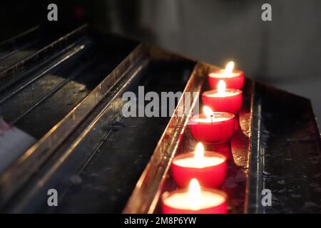 Una fila di candele di luce del tè che brucia in chiesa con fuoco su quella centrale. Foto Stock