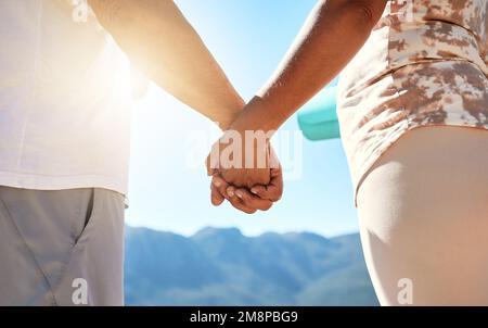 Primo piano di una coppia matura che tiene le mani e guarda la vista delle montagne mentre si pratica lo yoga all'aperto Foto Stock