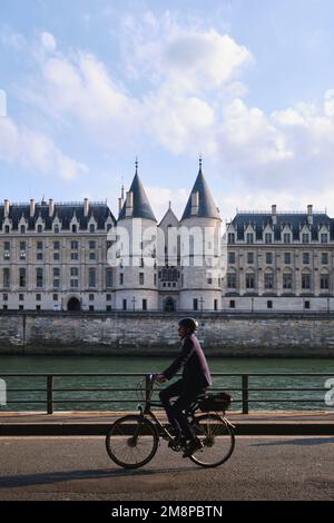 Parigi, Francia - Maggio, 2022: Un uomo in bicicletta sulle rive della senna di fronte a la Conciergerie, ex prigione trasformata in tribunali Foto Stock