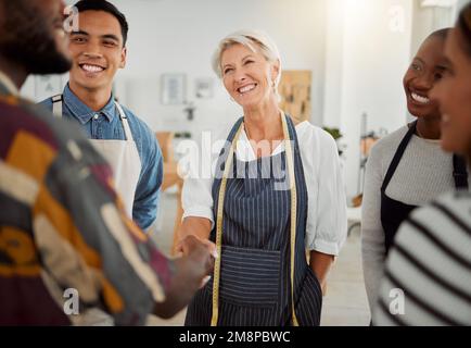 Gruppo di designer creativi diversi e felici che si incontrano mentre si trovano al lavoro. I colleghi salutano e scuotono le mani in un ufficio. Maschio Foto Stock