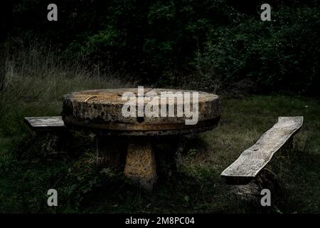 Un primo piano di un tavolo rotondo in pietra con panchine in legno fatte a mano in un parco verde Foto Stock