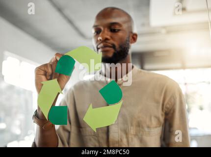Giovane uomo d'affari afroamericano focalizzato disegnare un simbolo di riciclaggio su una finestra di vetro in un ufficio sul lavoro. Un uomo d'affari serio progettazione Foto Stock