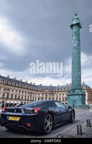 Parigi, Francia - Maggio, 2022: Vista della colonna di Vendome in piazza Vendome con auto super sportiva di lusso in una giornata nuvolosa Foto Stock