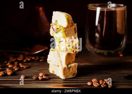Halva biologica con pistacchi su una superficie di legno. Dolci orientali tradizionali. Caffè fresco, cezve di rame e chicchi di caffè sparsi sullo sfondo Foto Stock