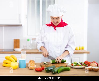 Donna proffesional cuoca in bianco uniforme tagliando verdure Foto Stock