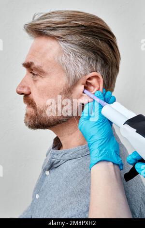 Stampi per orecchie, inserti auricolari e impronte. Processo di realizzazione di tappi per le orecchie e di stampi per le orecchie individuali per pazienti maschi in clinica auricolare con audiologo Foto Stock