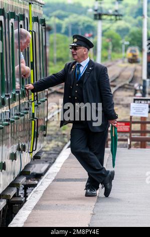 Una guardia ferroviaria chiacchiera con un passeggero a bordo di una DMU Bubblecarat BR Classe 122 alla stazione di Toddington nel Cotswolds, Gloucestershire, Gran Bretagna. Si tratta di pa Foto Stock