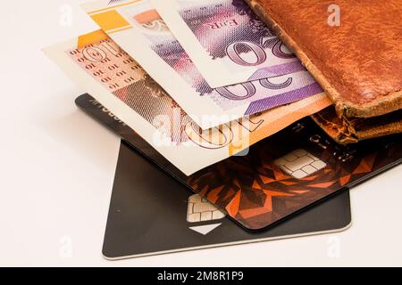 primo piano di un mucchio di banconote da dieci e venti sterline con un portafoglio in pelle marrone e una carta di credito nera Foto Stock