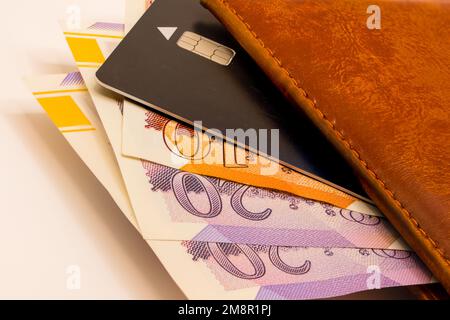 primo piano di un mucchio di banconote da dieci e venti sterline con un portafoglio in pelle marrone e una carta di credito nera Foto Stock