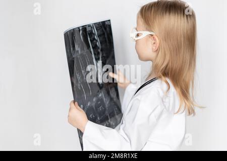 Medico con occhiali e stetoscopio, che tiene e guarda la pellicola radiografica di radiografia, scansione tc, MRI della colonna vertebrale. Neurologo al lavoro. Retro neutro Foto Stock