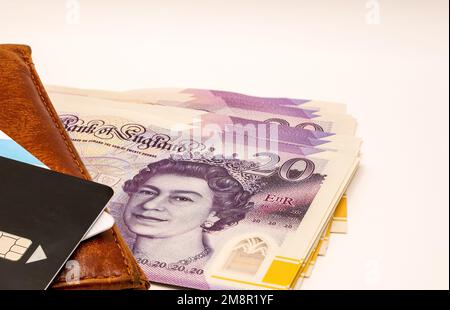 primo piano di un mucchio di banconote da dieci e venti sterline con un portafoglio in pelle marrone e una carta di credito nera Foto Stock
