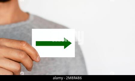 Uomo che tiene un segno di freccia a destra. Freccia verde rivolta verso destra. Il maschio. Direzione. Movimento. Dove. Foto Stock