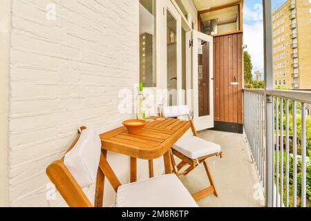 un balcone con due sedie e un tavolino sul lato sinistro del portico, che si affaccia sulla strada Foto Stock