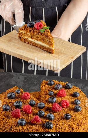 Uno chef femminile cuoce e mangia un pezzo di torta di carote fatta in casa su uno sfondo scuro. messa a fuoco selettiva Foto Stock