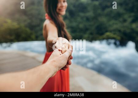 Primo piano di una donna che tiene la mano di un uomo vicino alla piscina. Concentratevi sulle mani della coppia. Scatto POV. Foto Stock