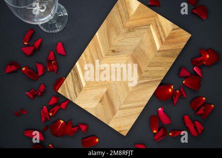 Tagliere in legno per cucinare su fondo nero scuro con un bicchiere di vino e petali di rosa rossa. Vista dall'alto. Foto Stock