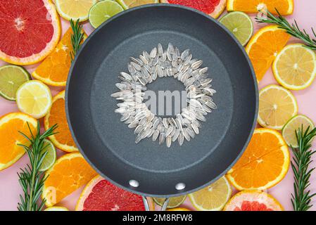 fondo delle fette di agrumi, arance, limoni, lime, pompelmi, su cui è posta una padella nera, all'interno della quale è fatto un girasole fr Foto Stock