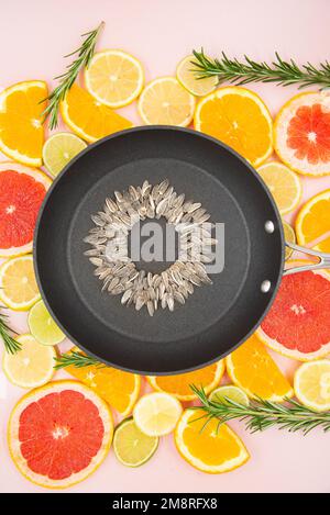 fondo delle fette di agrumi, arance, limoni, lime, pompelmi, su cui è posta una padella nera, all'interno della quale è fatto un girasole fr Foto Stock