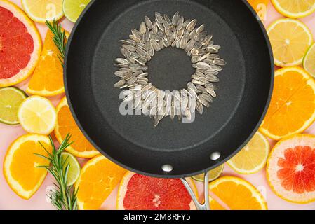 fondo delle fette di agrumi, arance, limoni, lime, pompelmi, su cui è posta una padella nera, all'interno della quale è fatto un girasole fr Foto Stock