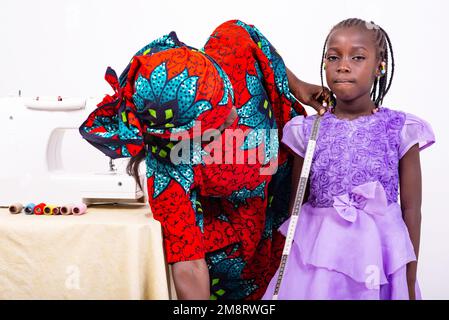 ritratto di una donna seamstress che misura il fondo di un vestito di bambina nella sua bottega. Foto Stock