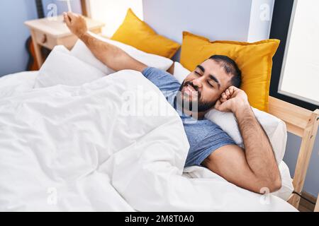 Giovane ispanico che si svegliò stendendo le braccia in camera da letto Foto Stock