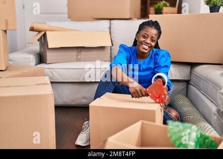 Donna afroamericana sorridente sicuro imballaggio scatola di cartone in nuova casa Foto Stock