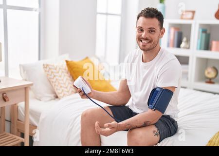 Giovane uomo ispanico che misura l'impulso usando il tensiometro in camera da letto Foto Stock