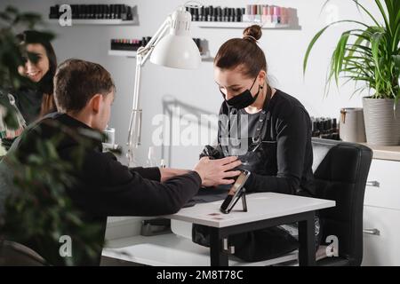 Manicure maschile. Maestro di servizio unghie femminile che fa manicure per l'uomo adulto. Uomo seduto nel salone di bellezza Foto Stock