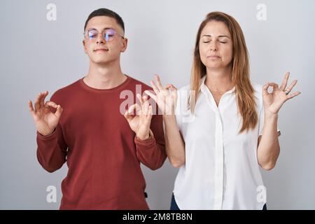 Madre e figlio in piedi insieme su sfondo isolato rilassato e sorridente con gli occhi chiusi facendo gesto di meditazione con le dita. concetto di yoga. Foto Stock