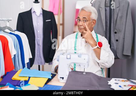 Uomo di mezza età con parrucchiere grigio utilizzando macchina da cucire puntando all'occhio che vi guarda gesto, espressione sospetta Foto Stock