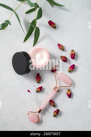 Crema viso e massaggiatore su sfondo chiaro. Il concetto di cura cosmetici con rosa e eucalipto. Salute e bellezza. Vista dall'alto. Foto Stock