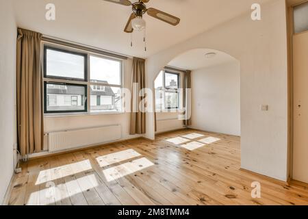 un soggiorno vuoto con pavimento in legno e ventilatore a soffitto nel centro della stanza è molto grandi finestre Foto Stock